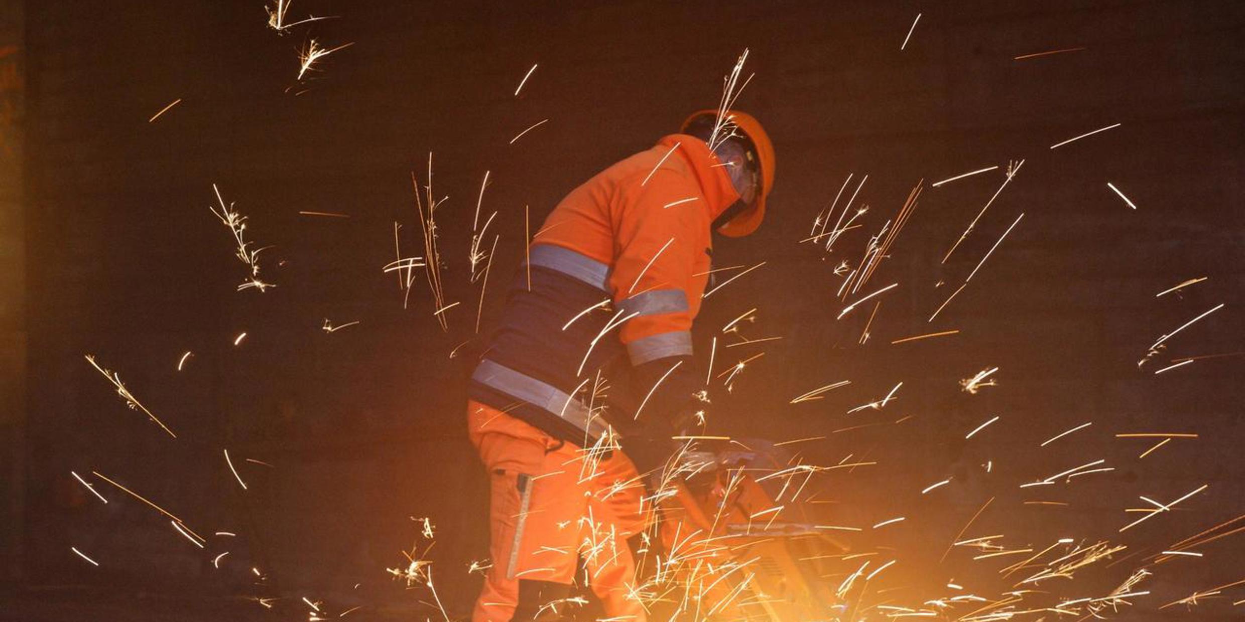 Ein SBB-Mitarbeiter in oranger Arbeitskleidung am schweissen